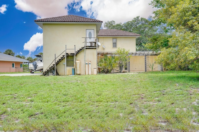 back of property featuring stucco siding, a lawn, a tiled roof, and stairs