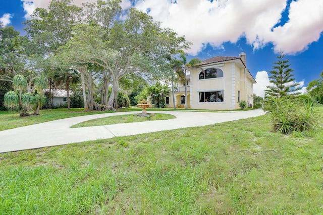 view of front facade featuring driveway, a chimney, a front yard, and stucco siding