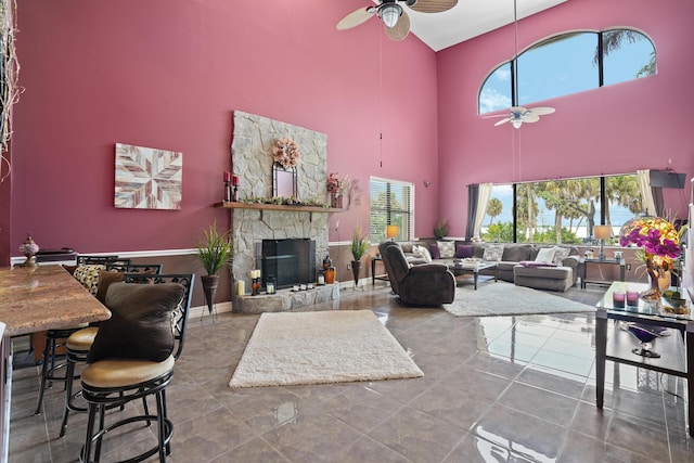 tiled living room with a ceiling fan, baseboards, a fireplace, and a high ceiling