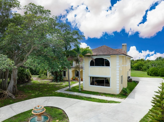 exterior space featuring a front lawn, a chimney, a tile roof, and stucco siding