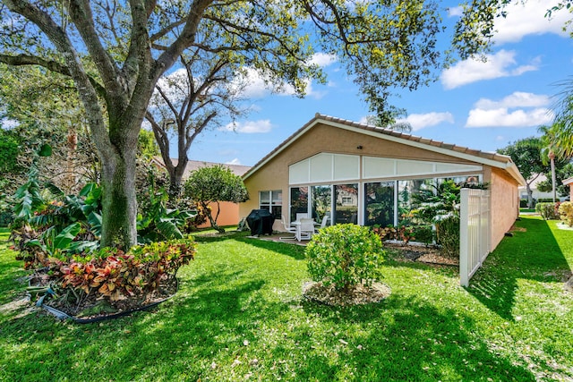 rear view of property featuring a sunroom, a lawn, and stucco siding