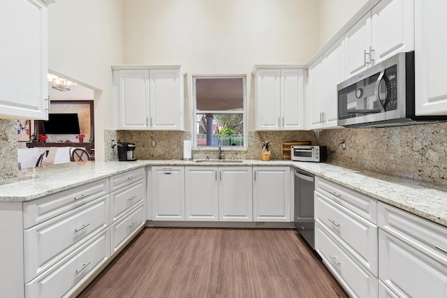 kitchen with tasteful backsplash, appliances with stainless steel finishes, white cabinets, a sink, and wood finished floors