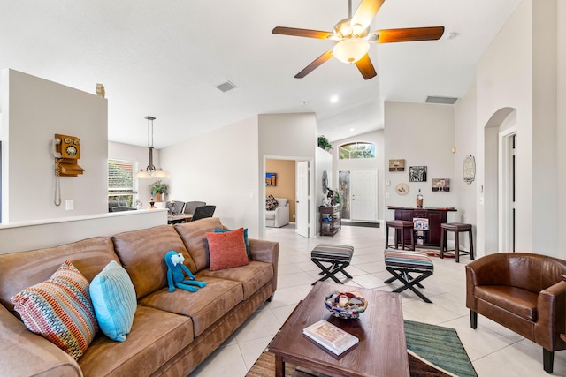 living room featuring light tile patterned floors, visible vents, arched walkways, ceiling fan, and high vaulted ceiling