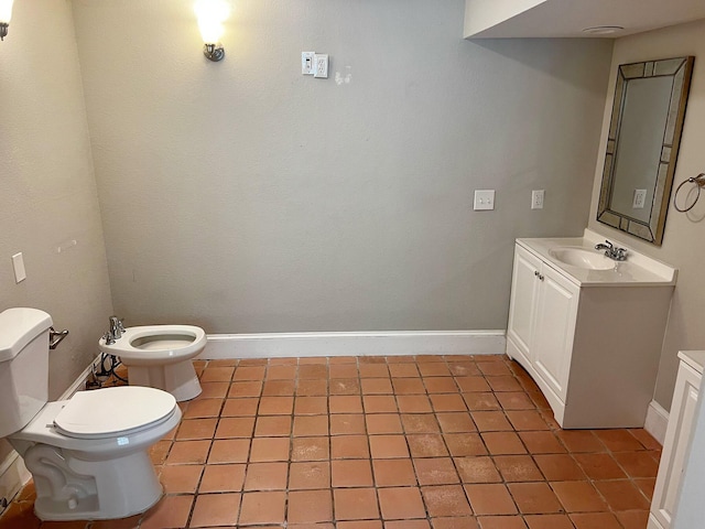 bathroom featuring toilet, vanity, baseboards, tile patterned floors, and a bidet