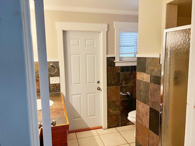 bathroom with a stall shower, toilet, tile patterned flooring, crown molding, and tile walls