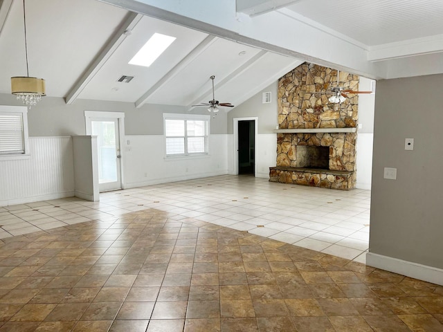 unfurnished living room with tile patterned flooring, wainscoting, a stone fireplace, and ceiling fan with notable chandelier