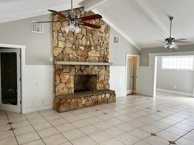 unfurnished living room with a ceiling fan, a wainscoted wall, visible vents, and a stone fireplace