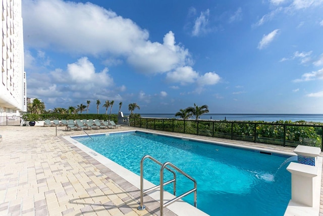 community pool with a patio, a water view, and fence