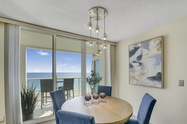 dining area featuring floor to ceiling windows, a water view, and a textured ceiling