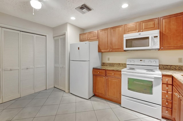 kitchen with light tile patterned floors, recessed lighting, white appliances, visible vents, and light stone countertops