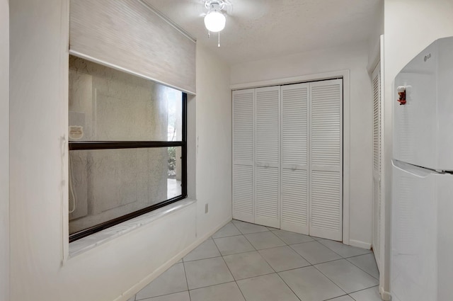 interior space with light tile patterned floors, baseboards, ceiling fan, freestanding refrigerator, and a closet