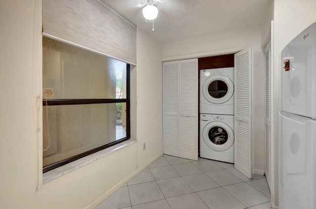 clothes washing area featuring stacked washer / dryer, laundry area, a textured ceiling, and light tile patterned floors