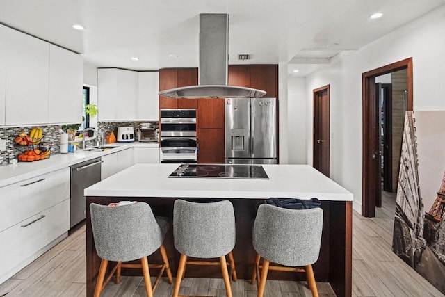 kitchen featuring a breakfast bar area, appliances with stainless steel finishes, a sink, island range hood, and modern cabinets