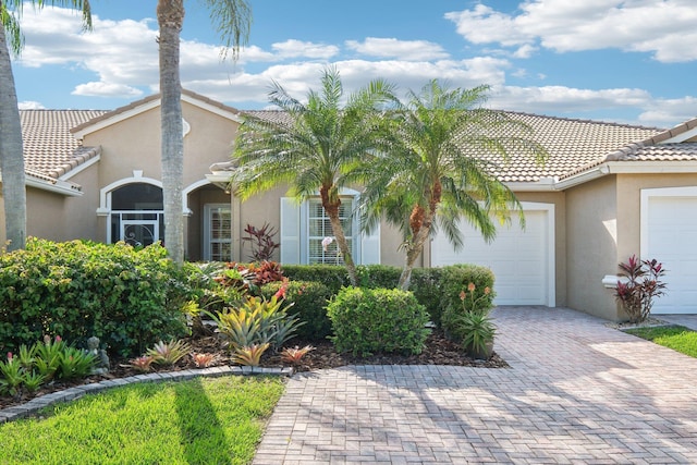 mediterranean / spanish-style house featuring an attached garage, a tiled roof, decorative driveway, and stucco siding