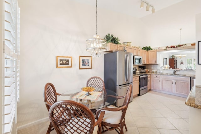 dining space with high vaulted ceiling, rail lighting, light tile patterned flooring, and a notable chandelier