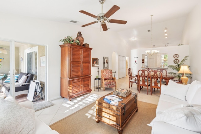 living area featuring visible vents, arched walkways, light tile patterned flooring, vaulted ceiling, and ceiling fan with notable chandelier