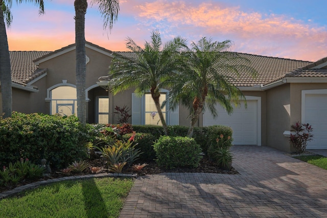 view of front of house with a garage, a tiled roof, decorative driveway, and stucco siding