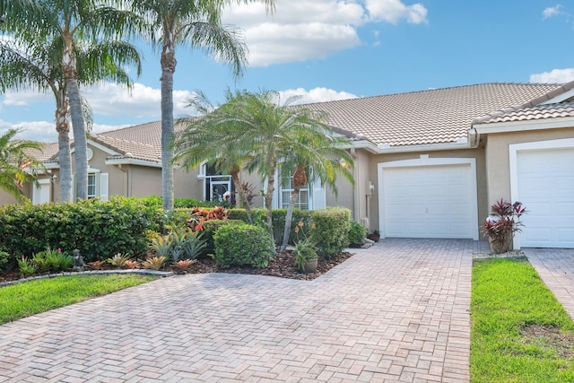 view of front facade featuring a garage, decorative driveway, a tile roof, and stucco siding