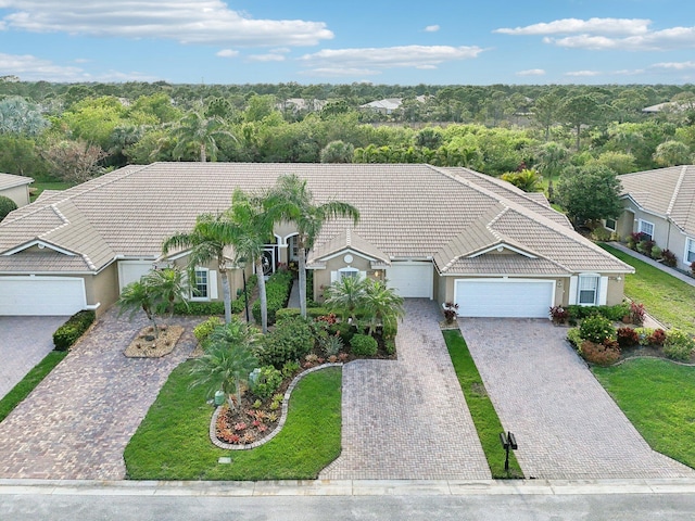 view of front of house featuring a tile roof, an attached garage, decorative driveway, a wooded view, and stucco siding