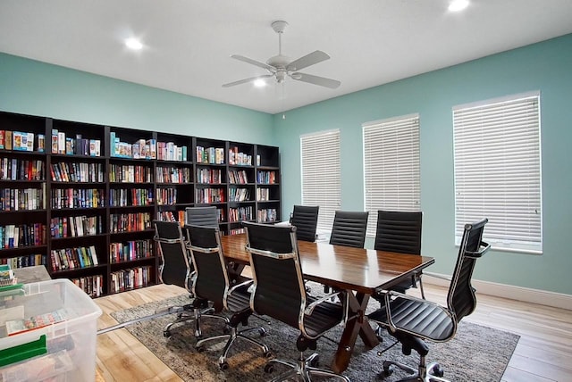 office area with bookshelves, ceiling fan, baseboards, and wood finished floors