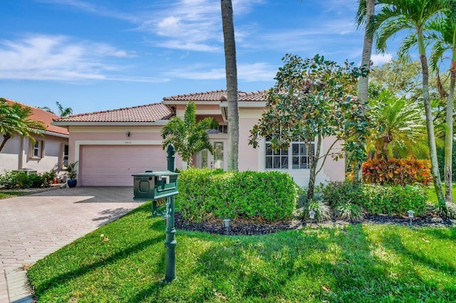 mediterranean / spanish-style home featuring decorative driveway, stucco siding, a garage, a tiled roof, and a front lawn