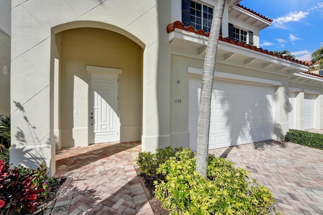 entrance to property with decorative driveway, a tile roof, an attached garage, and stucco siding