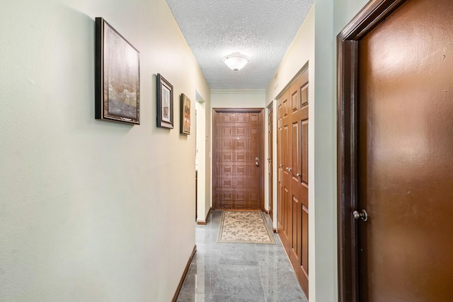 corridor featuring a textured ceiling and baseboards