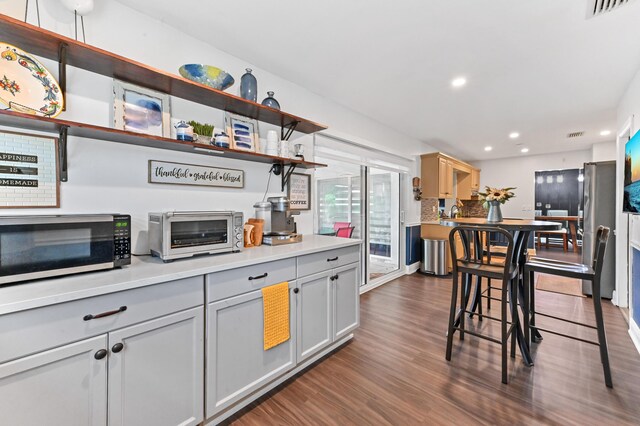 kitchen with a toaster, dark wood finished floors, stainless steel microwave, open shelves, and recessed lighting