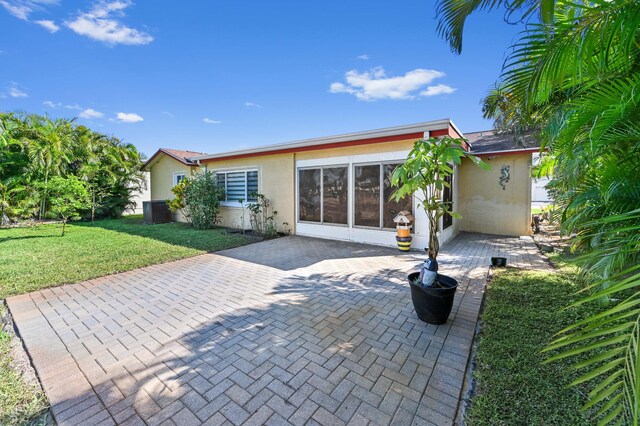 back of house with a yard, decorative driveway, a patio, and stucco siding