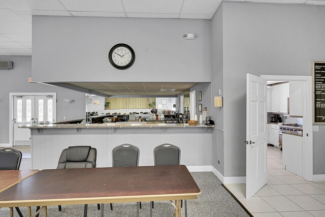 kitchen with a drop ceiling, baseboards, light tile patterned flooring, and white cabinetry