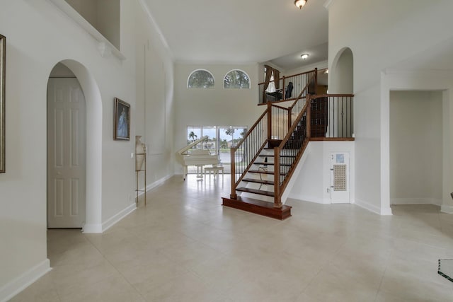 stairs with ornamental molding, arched walkways, a towering ceiling, and baseboards