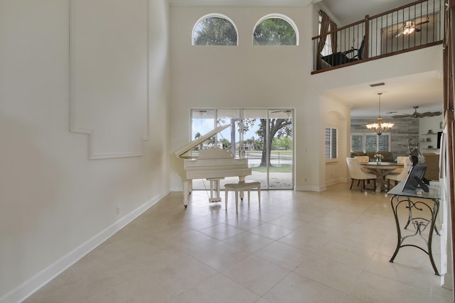 interior space with tile patterned flooring, a high ceiling, baseboards, and ceiling fan with notable chandelier