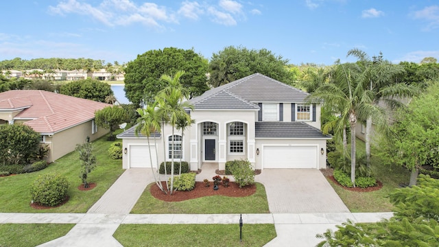 view of front facade with a tiled roof, decorative driveway, a front yard, and stucco siding