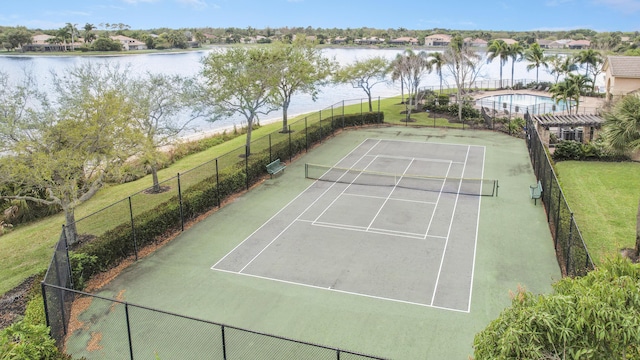 view of sport court featuring a water view, fence, and a yard