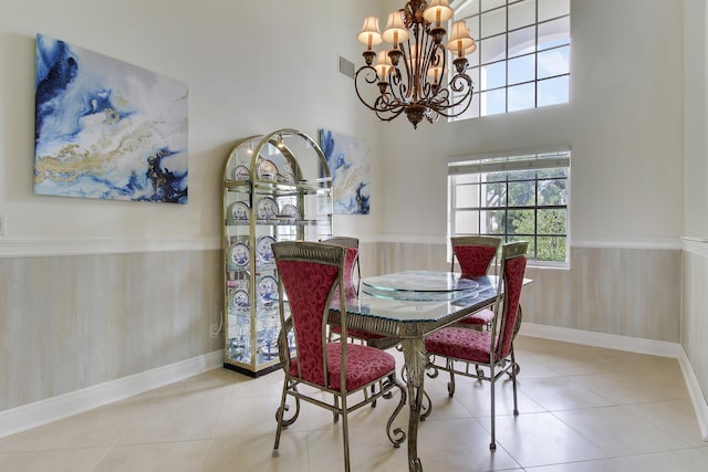 tiled dining space with visible vents, a towering ceiling, a wainscoted wall, wood walls, and a chandelier