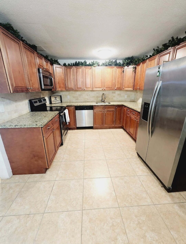 kitchen featuring a sink, appliances with stainless steel finishes, light tile patterned flooring, brown cabinetry, and light stone countertops