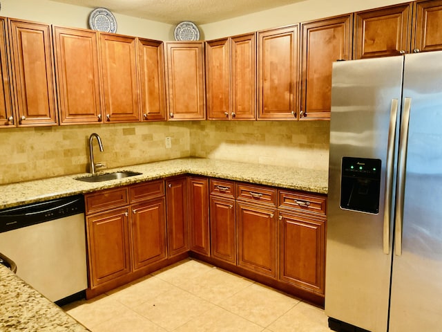 kitchen with backsplash, light stone counters, light tile patterned flooring, stainless steel appliances, and a sink