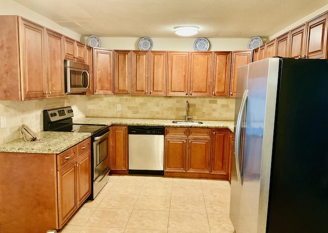 kitchen featuring brown cabinets, a sink, light stone counters, tasteful backsplash, and stainless steel appliances