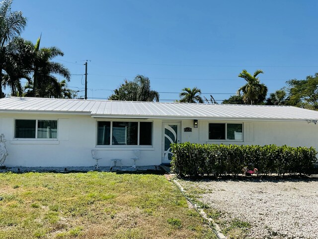 single story home with metal roof, a front lawn, and stucco siding