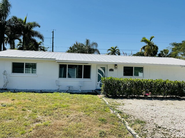 ranch-style house with metal roof, a front lawn, and stucco siding