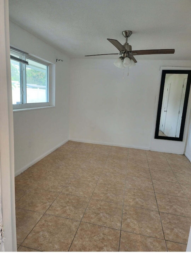 spare room with ceiling fan, tile patterned floors, baseboards, and a textured ceiling