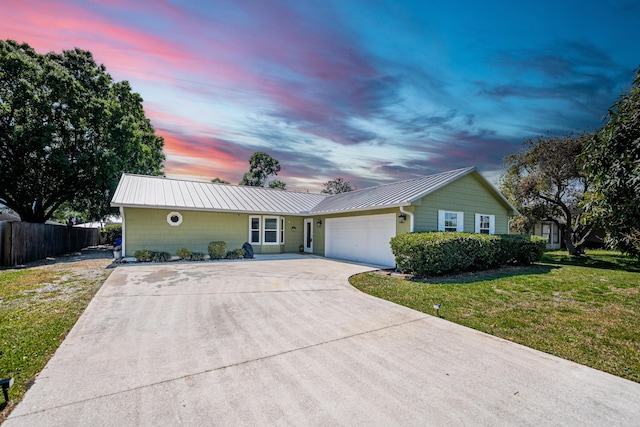 ranch-style home with a garage, fence, a yard, concrete driveway, and metal roof