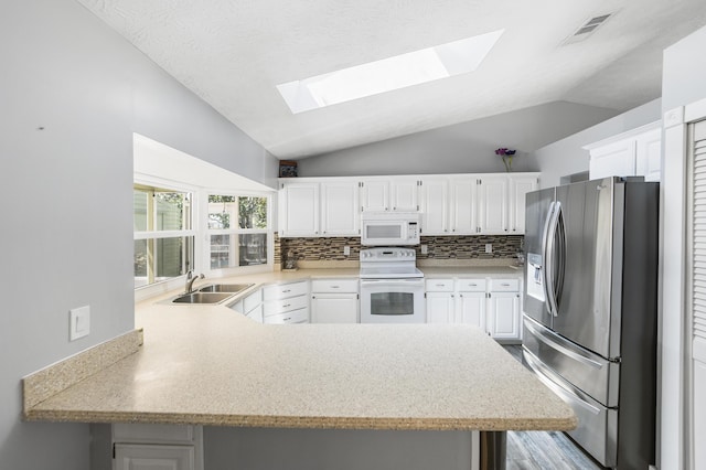 kitchen featuring visible vents, lofted ceiling with skylight, a peninsula, white appliances, and a sink