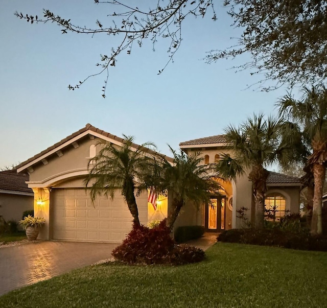 mediterranean / spanish home featuring an attached garage, a tile roof, stucco siding, a yard, and driveway