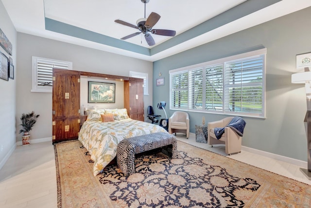 bedroom with wood finished floors, a tray ceiling, baseboards, and ceiling fan