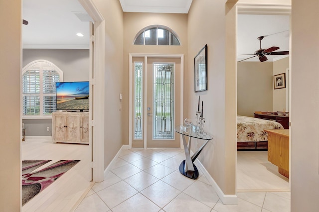 tiled entryway with ceiling fan, crown molding, and baseboards