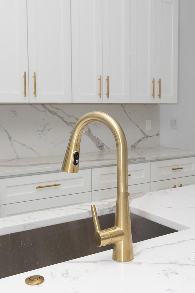 room details with a sink, light stone counters, white cabinets, and decorative backsplash