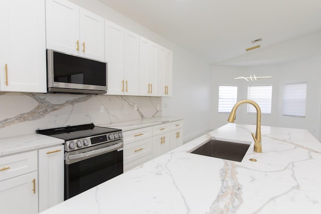kitchen featuring backsplash, lofted ceiling, stainless steel appliances, white cabinetry, and a sink
