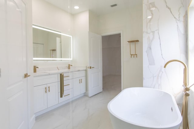 bathroom featuring double vanity, visible vents, marble finish floor, a freestanding bath, and a sink