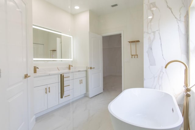 bathroom with visible vents, double vanity, a freestanding tub, marble finish floor, and a sink